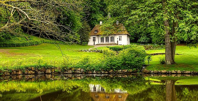 biały rustykalny domek nad jeziorem, otoczony lasem